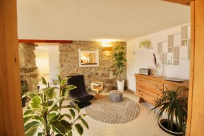 A living room with a stone wall, a black armchair, a wooden cabinet, and a round rug. - Les Cariolettes Lodge (Font-Romeu-Odeillo-Via)