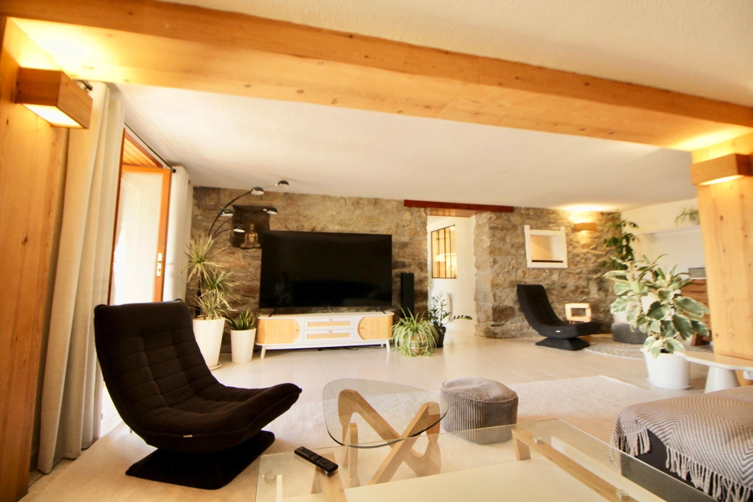 A modern living room with a black armchair, a glass coffee table, and a flat-screen TV mounted on a stone wall.
