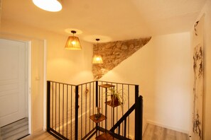 A staircase with a stone accent wall, a black railing, and a potted plant on the landing. - Les Cariolettes Lodge (Font-Romeu-Odeillo-Via)