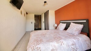 A hotel room with a bed, a TV mounted on the wall, and a door leading to a bathroom. - Les Cariolettes Lodge (Font-Romeu-Odeillo-Via)