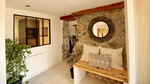 A modern interior with a stone wall, a round mirror, a wooden bench with cushions, and a potted plant. - Les Cariolettes Lodge (Font-Romeu-Odeillo-Via)