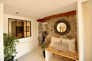 A modern interior with a stone wall, a round mirror, a wooden bench with cushions, and a potted plant. - Les Cariolettes Lodge (Font-Romeu-Odeillo-Via)