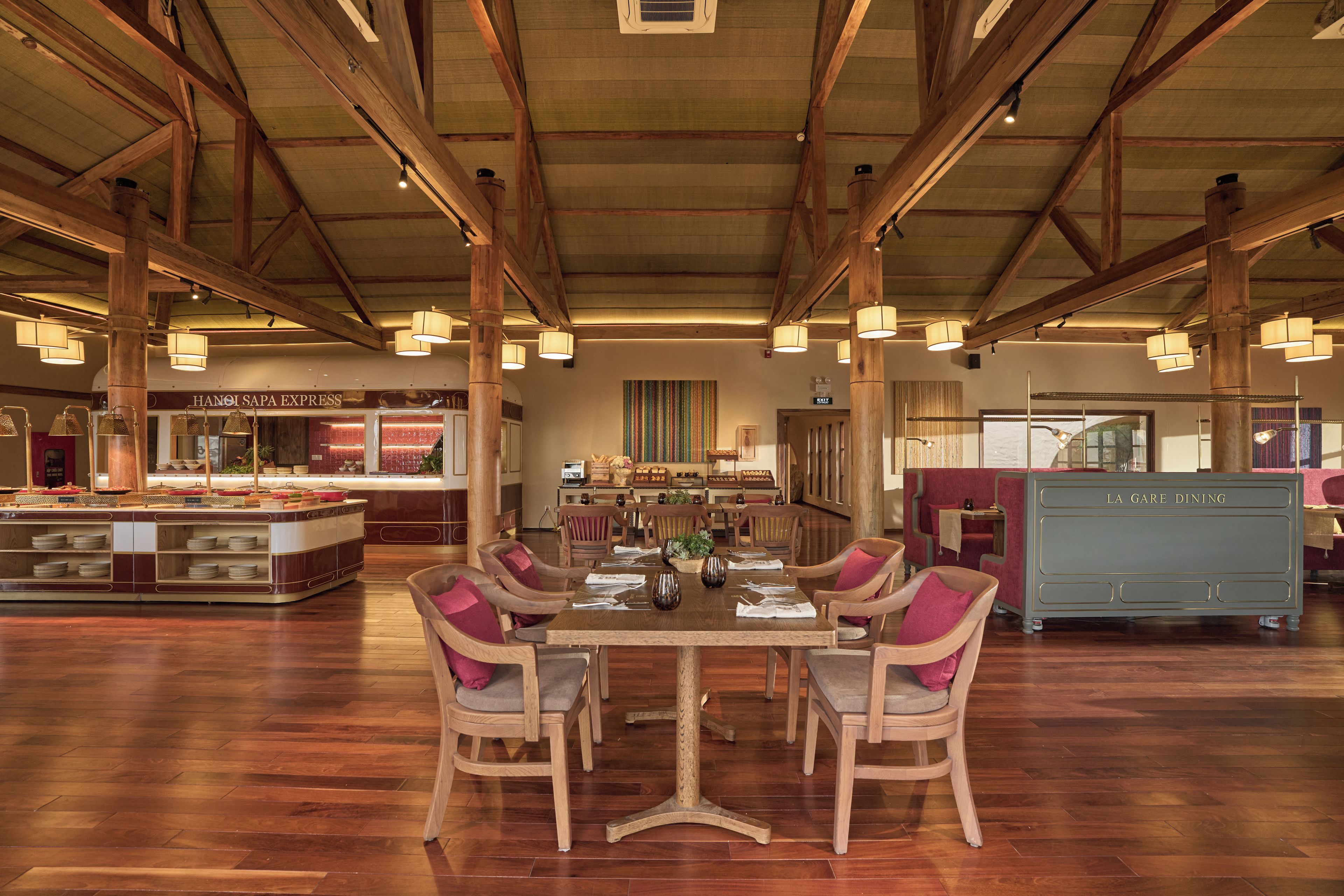 Ruime eetruimte met een hoge plafond en zichtbare houten balken, met een centrale tafel met stoelen en een buffet in de achtergrond.