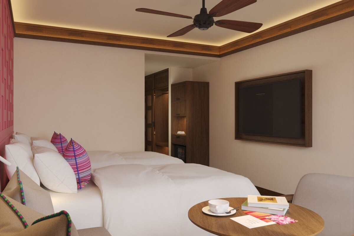 A hotel room with a bed, a seating area with a table, a ceiling fan, and a door leading to another room.