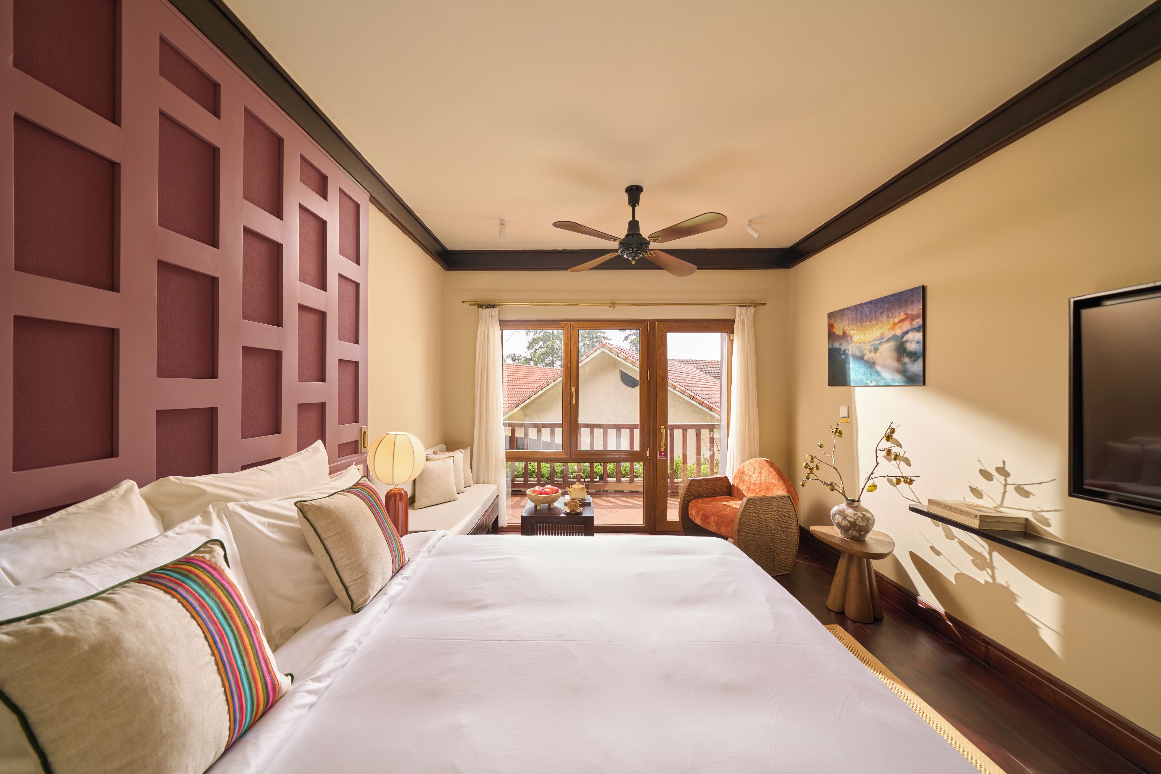 Una habitación de hotel con una cama grande, un ventilador de techo, un balcón con vistas y un cuadro en la pared.