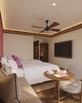 A hotel room with a bed, a seating area with a table, a ceiling fan, and a door leading to another room.