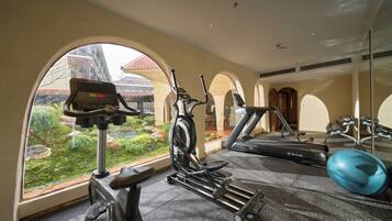 Un gimnasio con equipo de ejercicio, un ventanal y vista a un edificio de techo rojo.