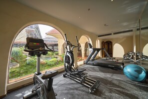 Un gimnasio con equipo de ejercicio, un ventanal y vista a un edificio de techo rojo.