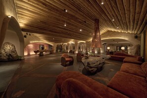 A spacious lobby with a high ceiling, stone walls, and a central seating area with sofas and a coffee table.