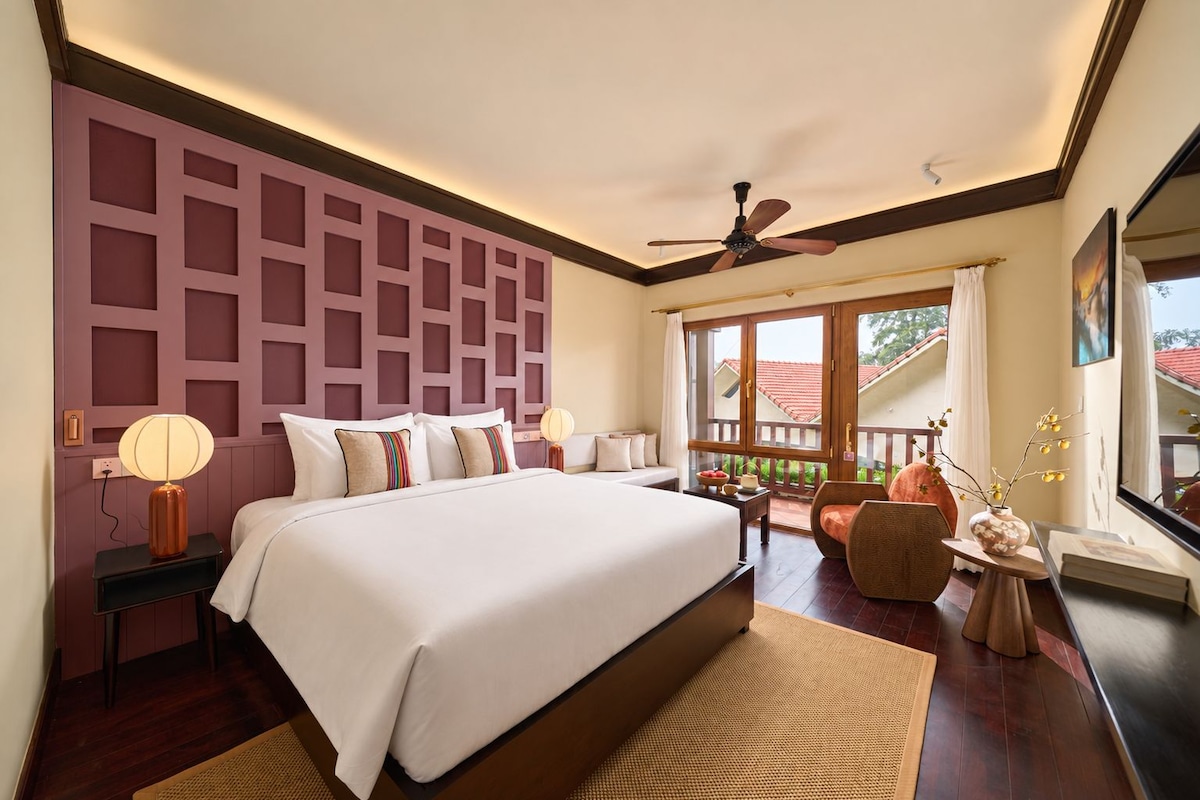 A bedroom with a large bed, a ceiling fan, a window with a view, and a balcony.