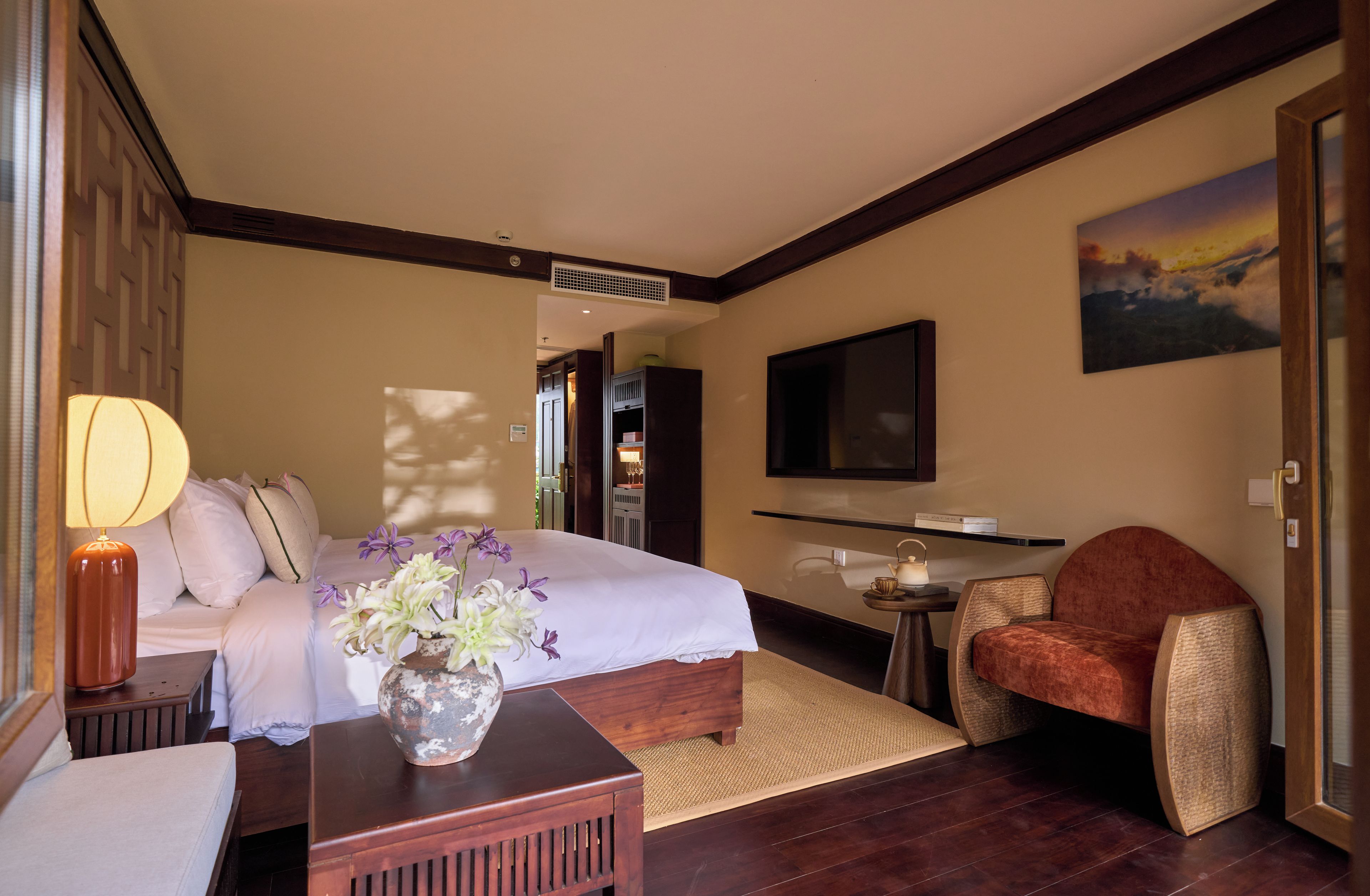 Habitación de hotel con cama, zona de estar con una silla, una mesita, televisor montado en la pared y un cuadro.
