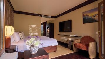 Habitación de hotel con cama, zona de estar con una silla, una mesita, televisor montado en la pared y un cuadro.