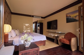 Habitación de hotel con cama, zona de estar con una silla, una mesita, televisor montado en la pared y un cuadro.