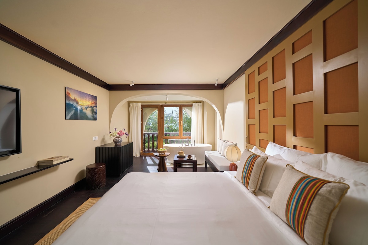 A hotel room with a large bed, a television, a desk, and a view of the outdoors.