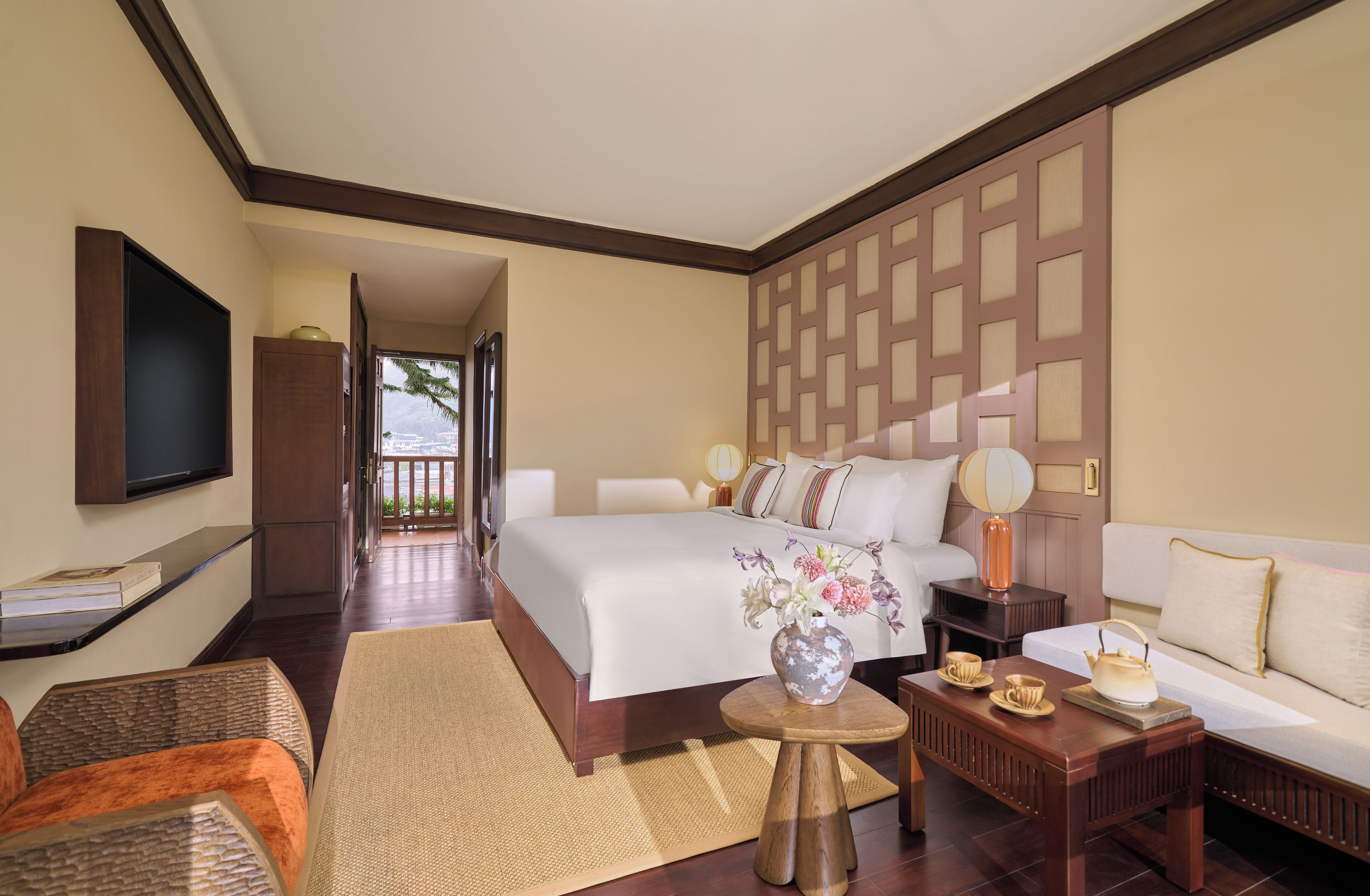 A hotel room with a large bed, a sofa, a TV, and a view of the outdoors.