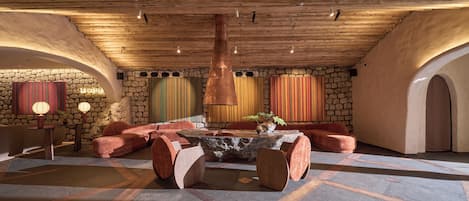 A cozy lounge area with a stone wall, wooden ceiling, and a central seating arrangement.