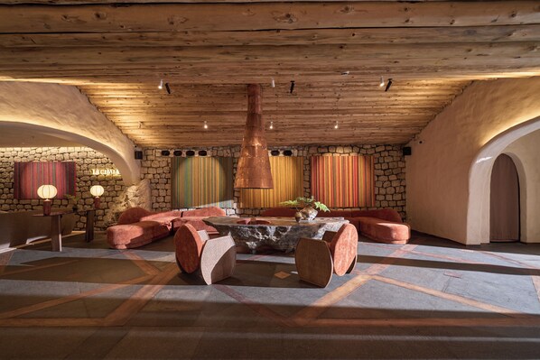 Un espacio de descanso acogedor con pared de piedra, techo de madera y una distribución central de asientos.