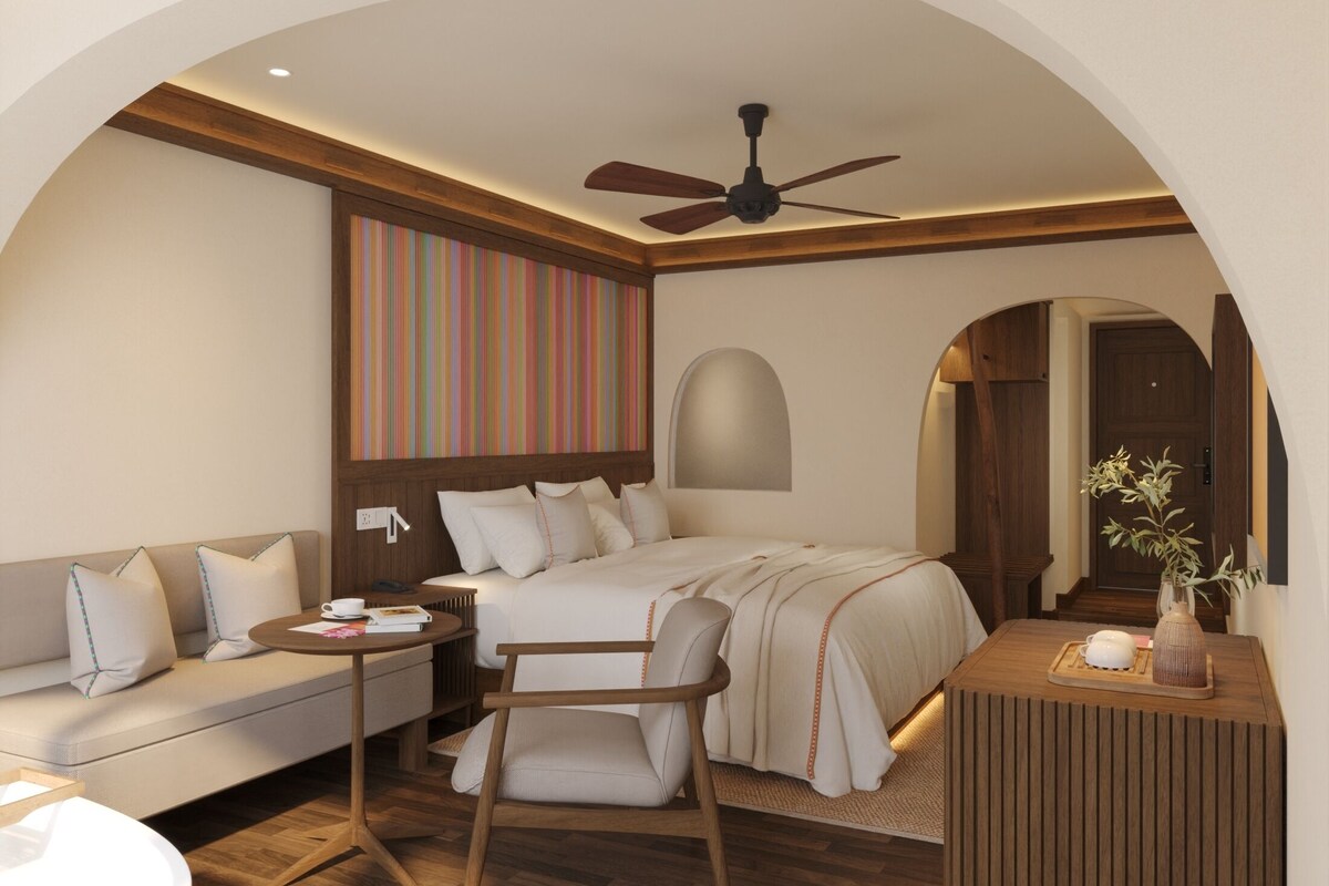 A hotel room with a bed, a sofa, a chair, a small table, and a ceiling fan.