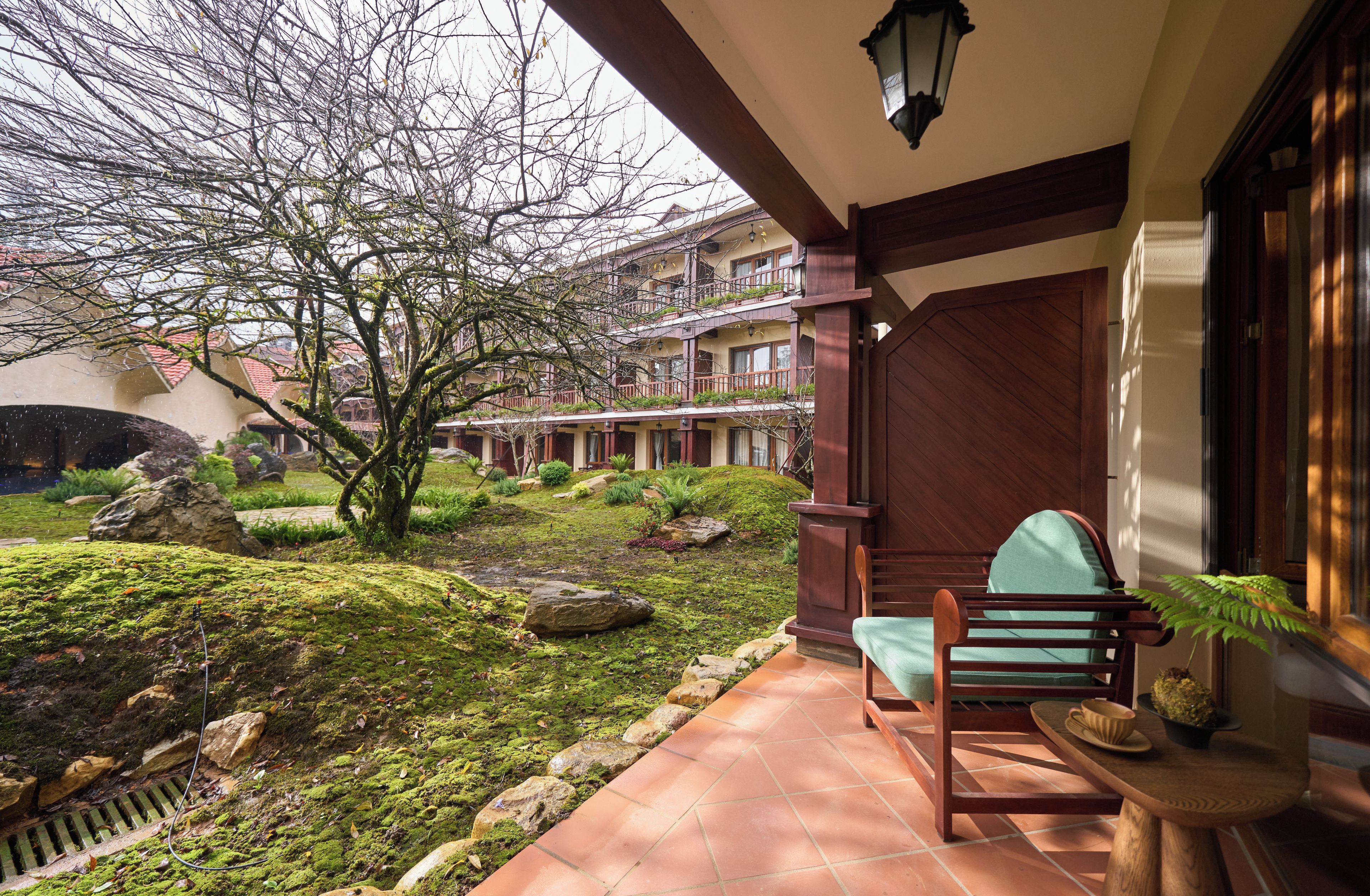 Ein traditionelles Gebäude mit einem Balkon, einem moosbewachsenen Garten und einem hölzernen Stuhl.