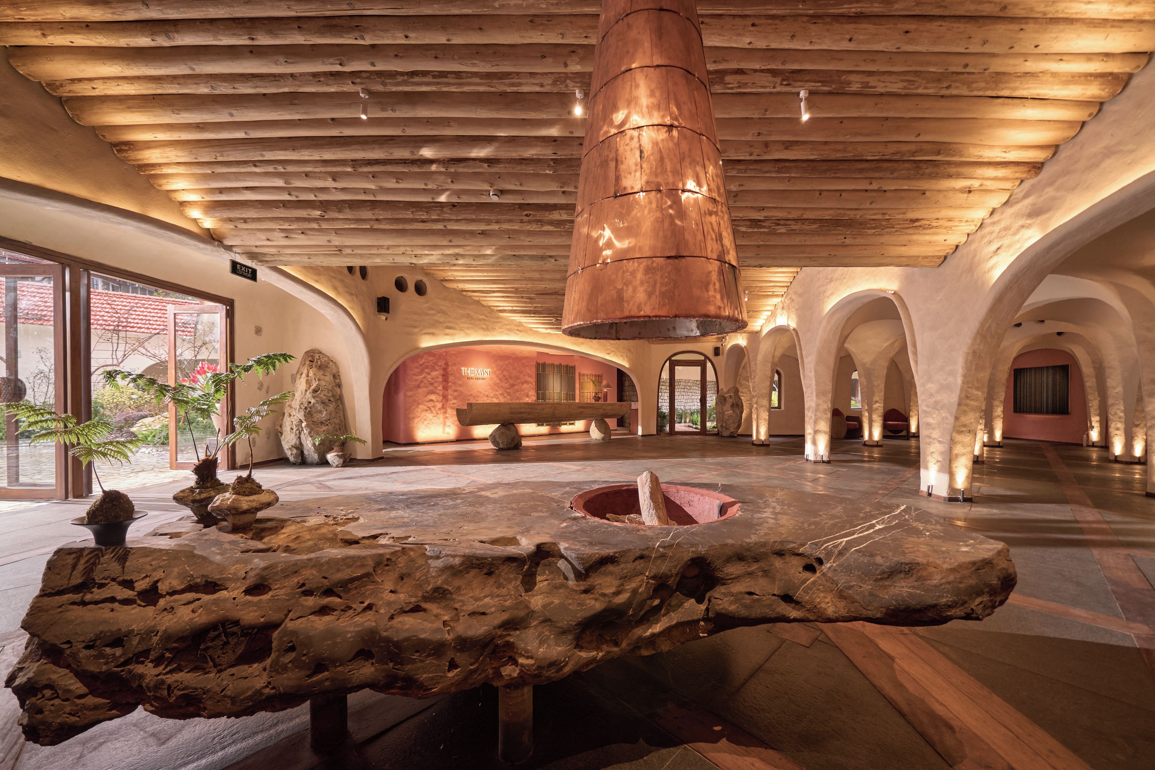 A spacious lobby with a wooden ceiling, a central stone feature, and a sign indicating an exit.