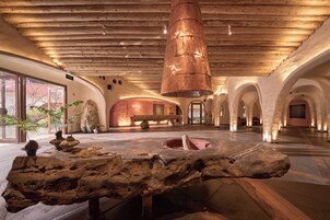 Un vestíbulo amplio con techo de madera, un elemento central de piedra y un cartel que indica una salida.