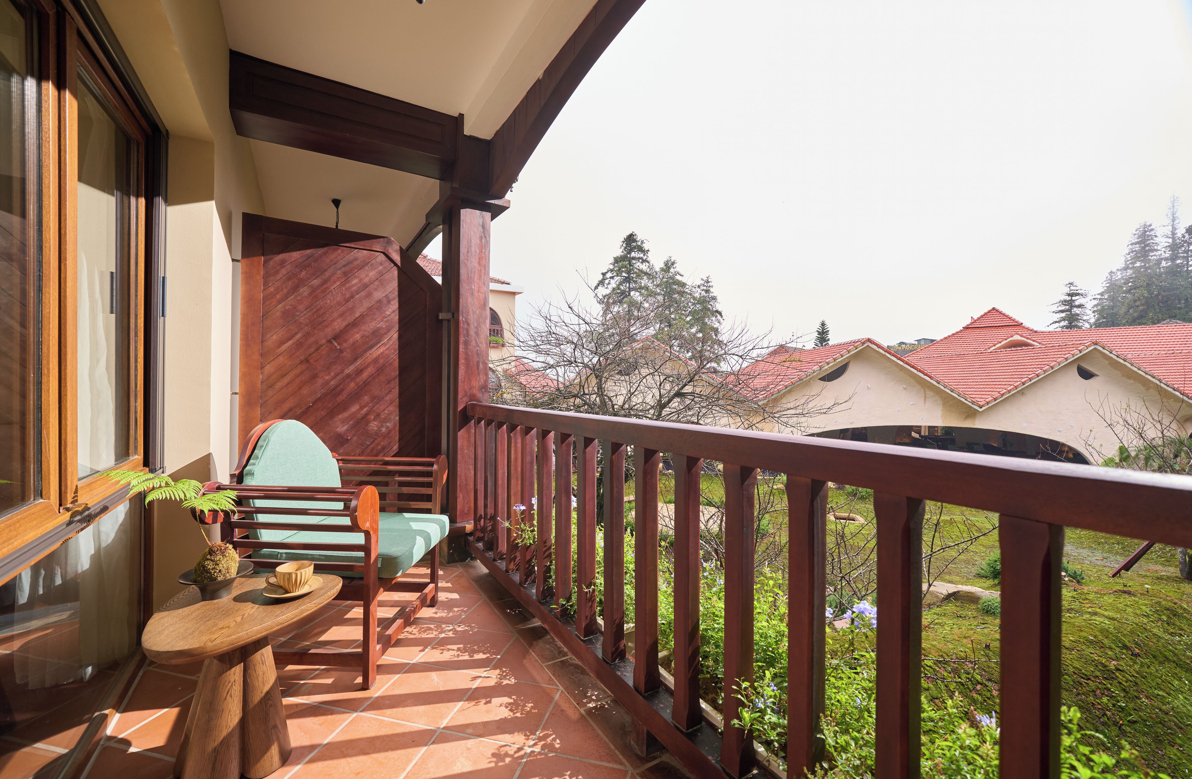 Un balcon avec une table et des chaises en bois, un pot de fleurs et une vue sur les maisons voisines.
