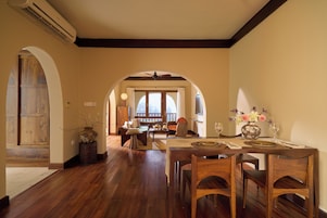 A dining area with a wooden table set for two, a vase with flowers, and a view through an archway to a balcony.