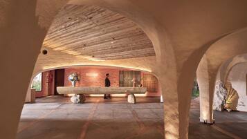 Un espacio interior con techo de madera, un banco de piedra y una pared con un arreglo floral.