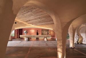 An interior space with a wooden ceiling, a stone bench, and a wall with a floral arrangement.