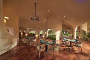 An interior with wooden flooring, tables, chairs, and a hanging chandelier.