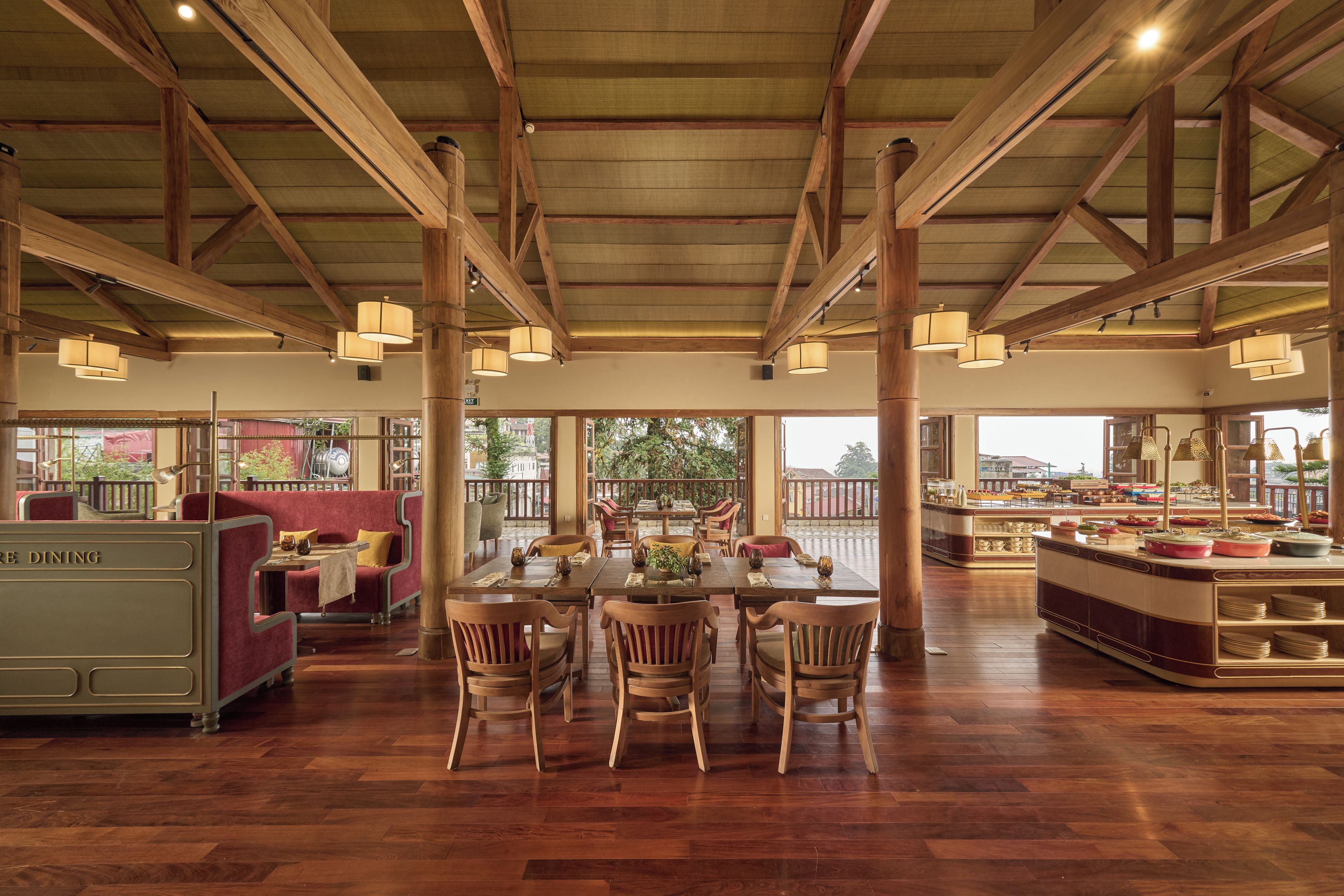 Un comedor amplio con mesas y sillas de madera, una barra de buffet y ventanas grandes que ofrecen vistas al exterior.