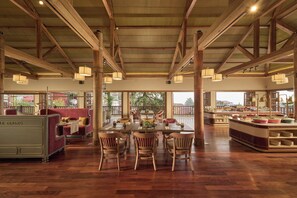 Un comedor amplio con mesas y sillas de madera, una barra de buffet y ventanas grandes que ofrecen vistas al exterior.