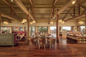 Un comedor amplio con mesas y sillas de madera, una barra de buffet y ventanas grandes que ofrecen vistas al exterior.