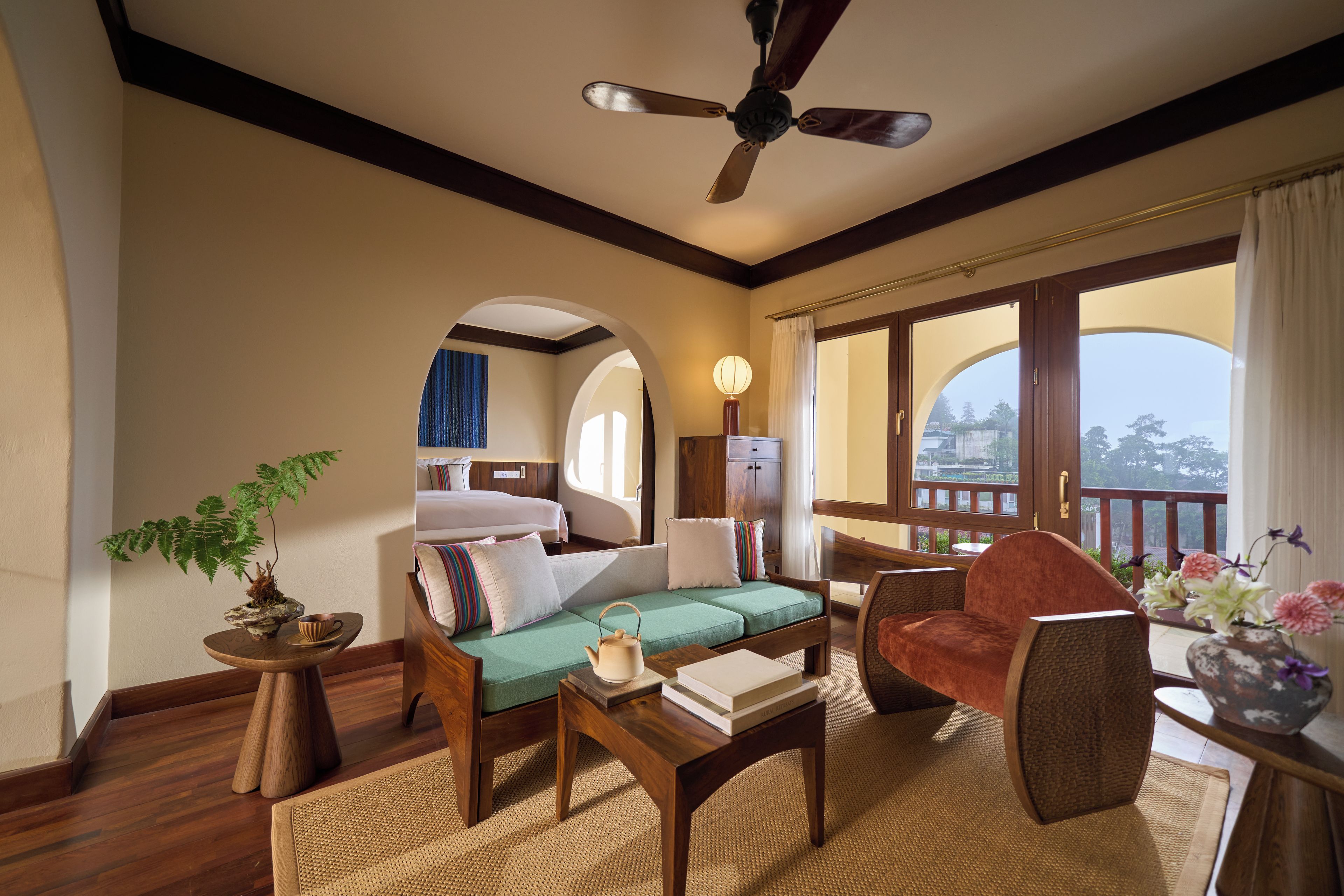 A room with a bed, a sofa, a chair, a table, a floor lamp, and a ceiling fan.