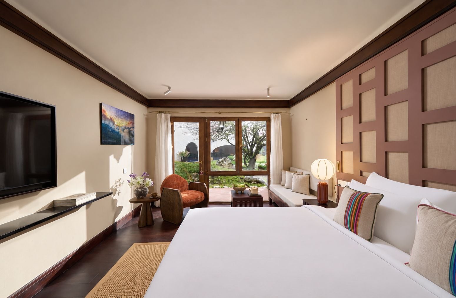 Habitación de hotel con una cama grande, televisión, sofá, sillón y vistas al exterior.