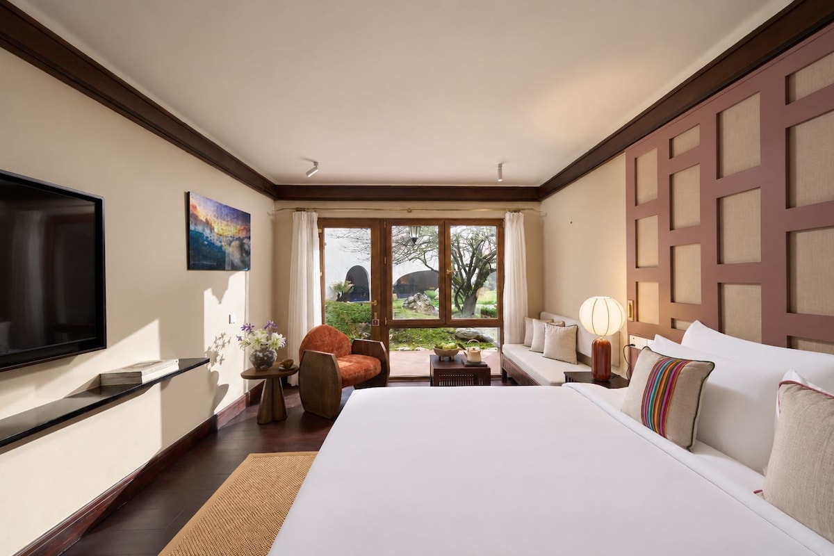 A hotel room with a large bed, a television, a sofa, a chair, and a view of the outdoors.
