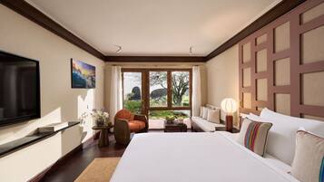 Habitación de hotel con una cama grande, televisión, sofá, sillón y vistas al exterior.