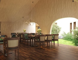 A spacious interior with wooden flooring, a central dining area with tables and chairs, and a large arched window providing a view of the outdoors.