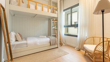 Dormitorio con literas, una silla de mimbre y una ventana con cortinas.