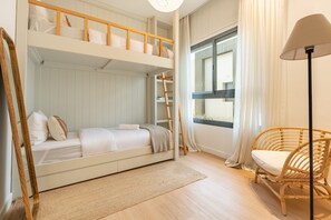 Dormitorio con literas, una silla de mimbre y una ventana con cortinas.