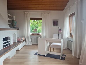 Ein Zimmer mit Kamin aus weißem Backstein, einem weißen Tisch und einem Fenster mit weißen Vorhängen.
