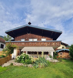 Ein zweistöckiges Holzhaus mit geneigtem Dach, einem Balkon und einer überdachten Veranda mit Sitzgelegenheit.
