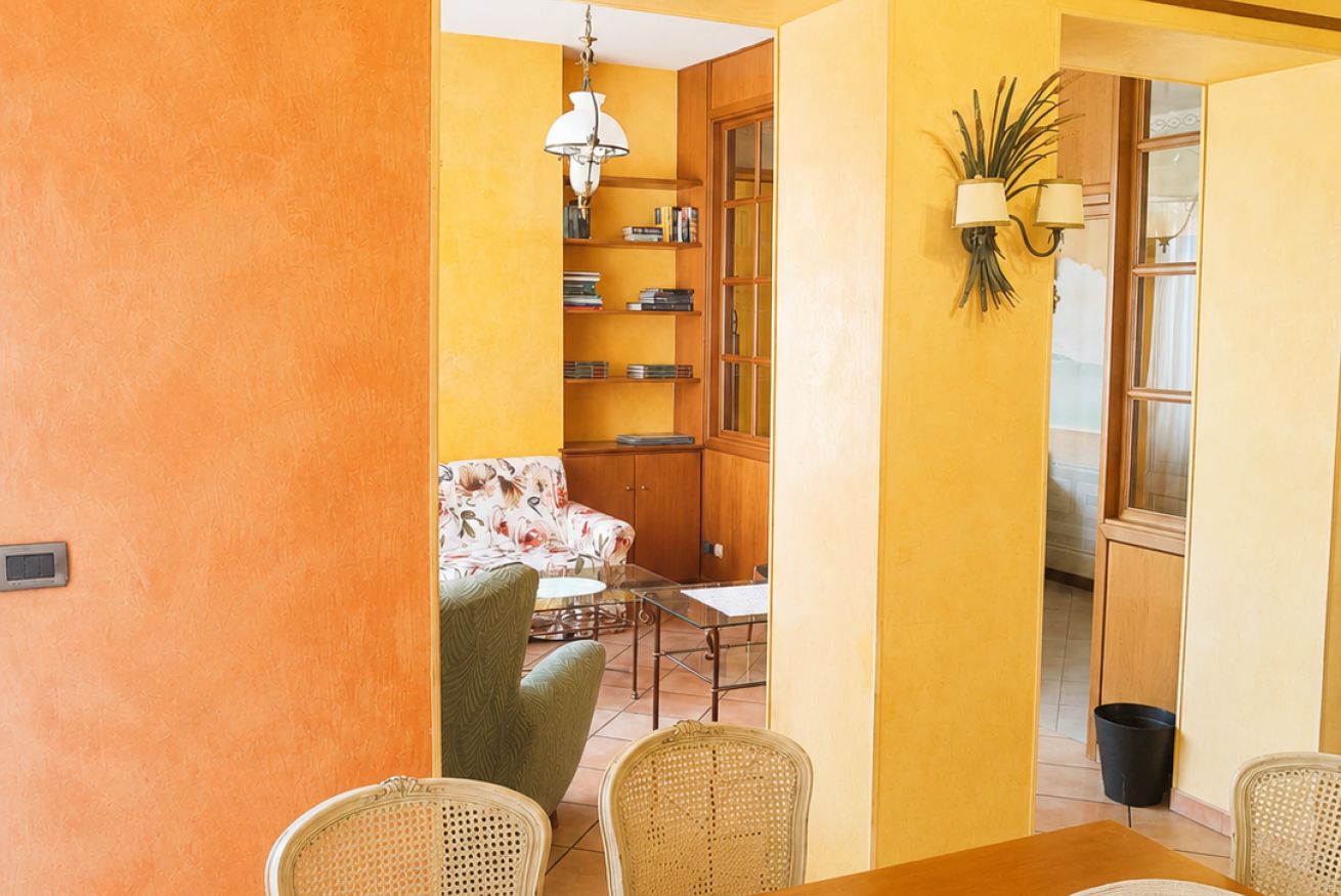 Ein Zimmer mit Esstisch, Stühlen, einer Couch, einem Bücherregal und einer Lampe.