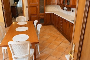 Un espace repas avec une table en bois et des chaises blanches, entouré d’armoires en bois et d’un comptoir blanc.
