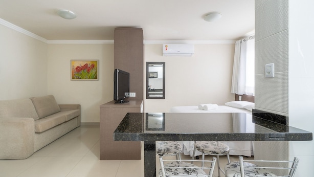 Habitación de hotel con sofá, escritorio con computadora, cama con edredón blanco y baño con cortina de ducha.