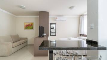 A hotel room with a sofa, a desk with a computer, a bed with a white comforter, a bathroom with a shower curtain, and a tiled wall.