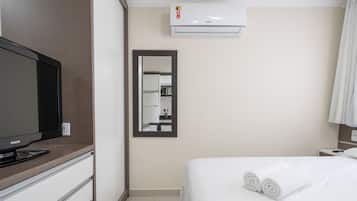 A hotel room with a bed, a television, a mirror, and an air conditioning unit.