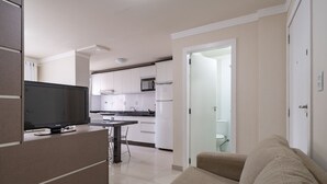 Una sala de estar moderna con un televisor de pantalla plana, un sofá y una cocina al fondo.
