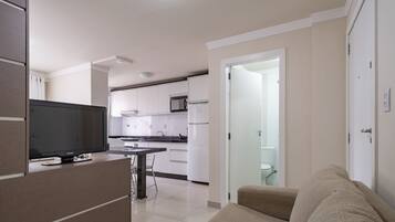 A modern kitchen with white cabinets, a flat-screen TV, and a dining area with a table and chairs.