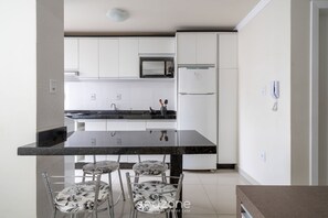 A modern kitchen with white cabinets, a black countertop, and a dining area with four chairs. - Studio 2min From Beach BC Close to Attrac. Eac1304 (Balneário Camboriú)